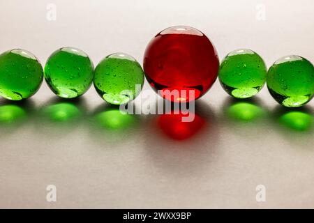 Una fila di marmi traslucidi verdi con un marmo traslucido rosso più grande. Foto Stock