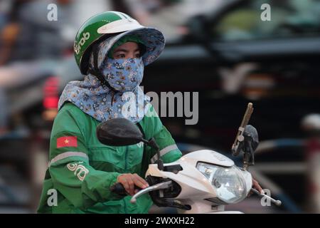 "Grab" - un'app di consegna - donna mascherata, su uno scooter, vista laterale nel traffico, ho chi min City (Saigon), Vietnam marzo 2024 Foto Stock