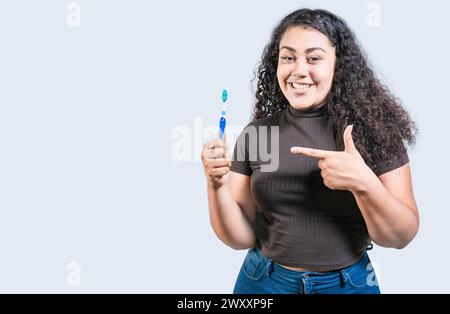 Donna sorridente che tiene e punta uno spazzolino da denti. Ragazza felice che tiene e punta lo spazzolino isolato Foto Stock