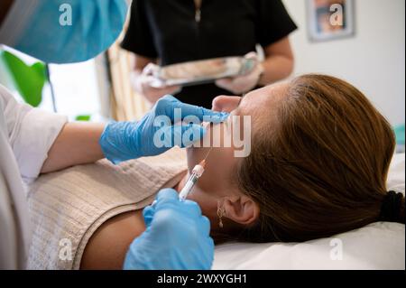 Specialista di bellezza che applica il prodotto cosmetico con la siringa sul viso del cliente in clinica Foto Stock