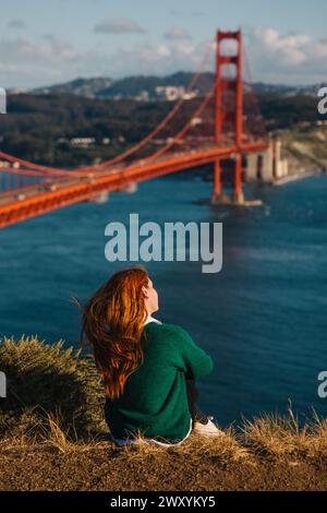 Una donna siede in contemplazione, guardando il Golden Gate Bridge e lo skyline di San Francisco, immersa nella bellezza della primavera Foto Stock