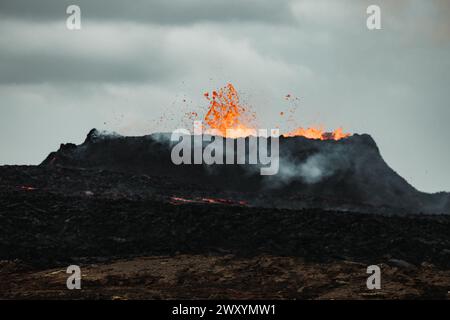 Una scena drammatica di un'eruzione vulcanica in Islanda, con lava luminosa che si proietta contro un cielo buio. Foto Stock