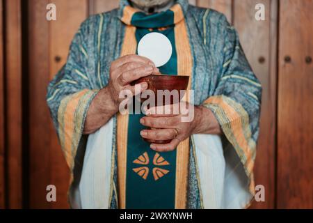 Il sacerdote anonimo eleva l'esercito eucaristico sopra un calice, un rituale centrale nella celebrazione del servizio della Comunione Cristiana Foto Stock