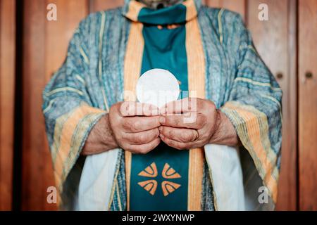 Primo piano delle mani anonime del sacerdote che presentano l'ospite eucaristico, un simbolo sacro nella Santa Comunione cristiana Foto Stock