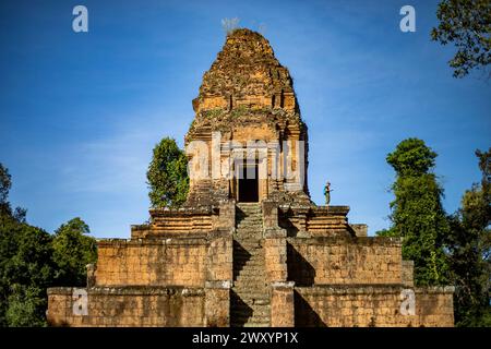 Un turista si erge in cima alle antiche rovine di Angkor Wat, ammirando la bellezza storica dell'iconico complesso di templi della Cambogia, sotto cieli azzurri. Foto Stock