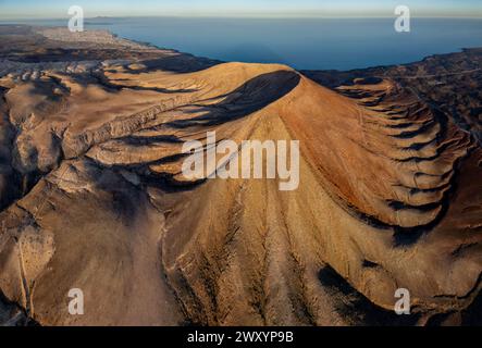 Il sole che tramonta illumina le creste di un maestoso vulcano sull'isola di Fuerteventura, con l'Oceano Atlantico che fornisce uno sfondo mozzafiato Foto Stock