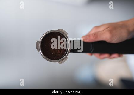 Immagine ravvicinata che mostra la mano di una persona che tiene in mano un portafiltro pieno di caffè appena macinato, pronto per l'estrazione dell'espresso Foto Stock