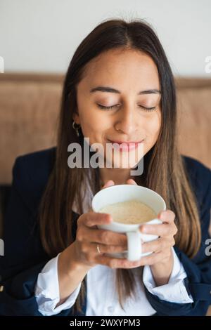 Una giovane donna apprezza l'aroma di un caffè fresco a occhi chiusi, assaporando il momento Foto Stock