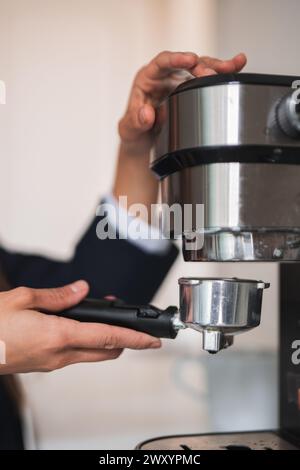 Primo piano tra le mani di un barista, che blocca sapientemente un portafiltro in una macchina da caffè professionale, preparandosi a preparare un caffè fresco Foto Stock