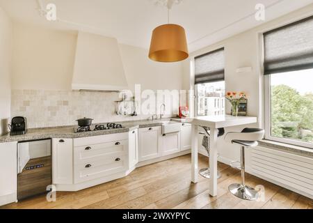 Una cucina moderna e ariosa, ben illuminata, con armadi bianchi, pavimenti in legno e un ripiano in granito, impreziosito da un elegante ciondolo arancione Foto Stock
