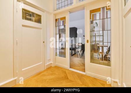 Vista di un'elegante zona pranzo attraverso porte francesi con pannelli di vetro, che mostrano un design moderno con pavimento in legno a spina di pesce. Foto Stock