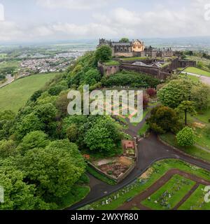 Panorama droni del Castello di Stirling, circondato da giardini lussureggianti e da un antico cimitero con il tranquillo paesaggio scozzese che si estende in lontananza Foto Stock