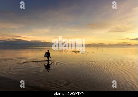 Kourou, spiaggia "plage de Lance", Guyana francese: Un pescatore cammina in acqua per sollevare le reti in acque calme la mattina Foto Stock