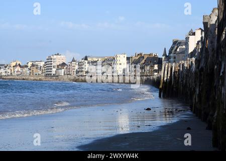 Tronchi d'albero si tuffavano nella spiaggia sabbiosa come frangiflutti di fronte al lungomare, Francia, Bretagna, Saint-Malo Foto Stock