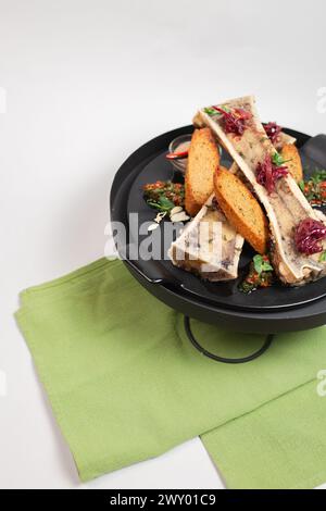 vista dall'alto delicata, midollo osseo cotto con crostini, erbe e spezie su un piatto nero. Foto Stock
