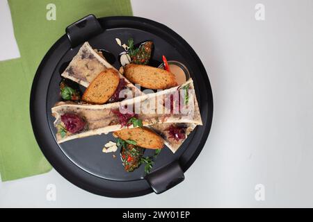 vista dall'alto delicata, midollo osseo cotto con crostini, erbe e spezie su un piatto nero. Foto Stock