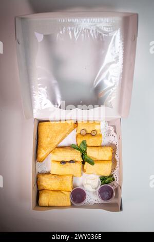 Un assortimento di deliziosi pasticcini e contorni in una scatola, tra cui pancake e una varietà di salse e marmellate. Foto Stock