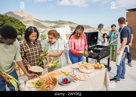 Persone multigenerazionali che fanno barbecue sul tetto di casa - amici multirazziali che si divertono a mangiare e cucinare insieme durante il giorno del fine settimana - estate e.. Foto Stock