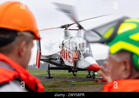 Steinach, Germania. 3 aprile 2024. I lavoratori forestali osservano il rifornimento dell'elicottero speciale con la testa della mietitrice su un cavo di sospensione durante un'operazione su un pendio ripido nell'ufficio forestale di Sonneberg. Questa è la prima volta che in Germania viene utilizzata questa speciale tecnologia assistita da elicotteri, con Thüringen Forst che la utilizza per proteggere la strada sottostante dal pericolo di caduta delle cime degli alberi su due ettari. I faggi sono caduti vittime della siccità degli ultimi anni. Credito: Michael Reichel/dpa/Alamy Live News Foto Stock