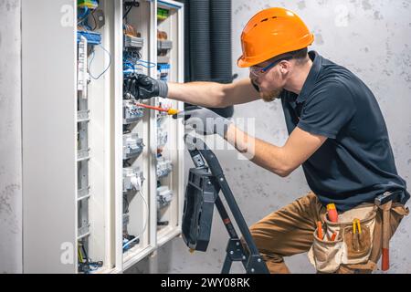 Giovane elettricista adulto ingegnere civile avvitando l'apparecchiatura nella scatola fusibili. Foto Stock