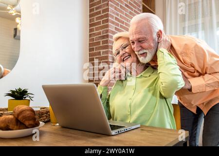 Una coppia di anziani sorridente che utilizza un notebook a casa in salotto. Foto Stock