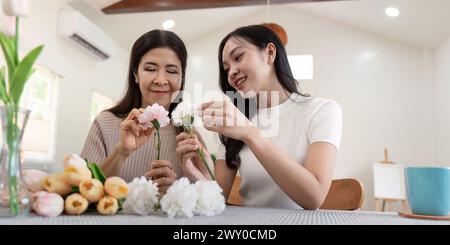 Madre anziana e figlia adulta felici sul tavolo mentre sistemano i fiori in un vaso insieme. Tecnologia e stile di vita. Buon tempo insieme Foto Stock