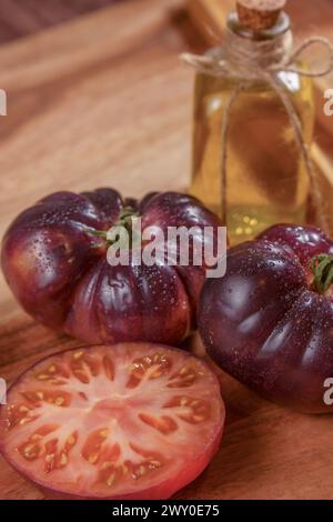 Un gruppo di pomodori blu con un pomodoro tagliato a metà con una bottiglia di olio d'oliva e alcune pinze di legno su un tavolo di legno Foto Stock