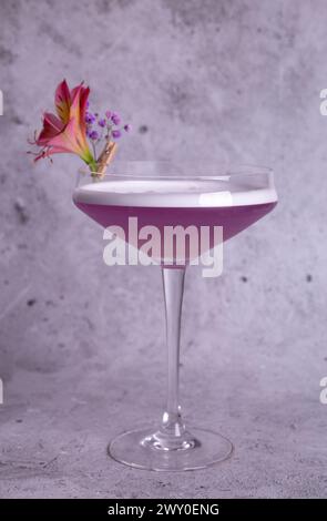 Elegante immagine di un cocktail rosa in un bicchiere con decorazione floreale su sfondo grigio, trasuda classe e raffinatezza. Foto Stock