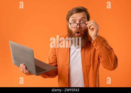 l'uomo con la barba regge il look di un notebook con un'espressione sconvolgente, studio Foto Stock