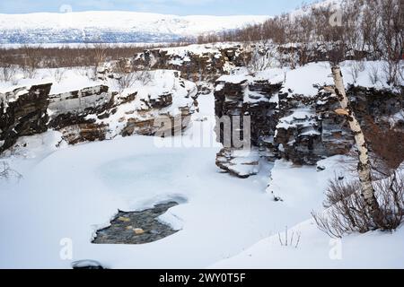 Paesaggio artico di neve, ghiaccio, acqua e ripide pareti rocciose presso la Gola del fiume Abisko nel Parco Nazionale di Abisko, Svezia. Foto Stock