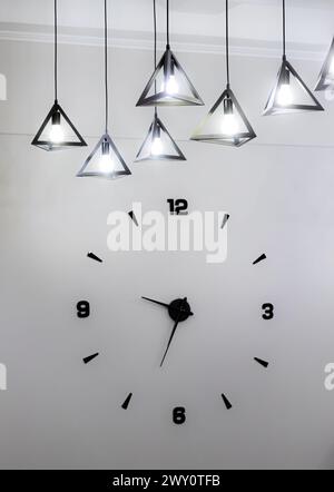 Design minimalista di un orologio da parete con numeri neri e una lampadina. Foto Stock