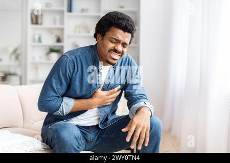 Giovane uomo Nero che prova dolore al torace nel salotto Foto Stock