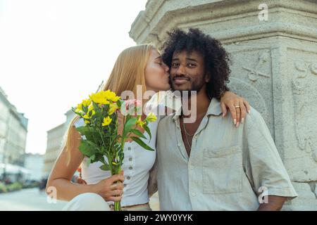 Il fidanzato riceve un bacio dalla sua ragazza dopo averle dato un mazzo di fiori, coppia mista. Foto Stock