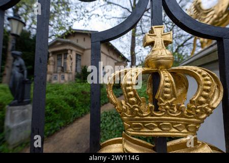 Potsdam, Germania. 3 aprile 2024. Un cancello d'ingresso con una corona dorata e la piccola portineria del Palazzo Glienicke, che fa parte della Fondazione dei Palazzi e dei Giardini prussiani Berlino-Brandeburgo (SPSG). Nel corso della tradizionale conferenza stampa annuale del 5 aprile 2024, il bilancio dell'anno passato e i piani della fondazione saranno presentati. Credito: Soeren Stache/dpa/Alamy Live News Foto Stock