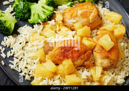 cosce di pollo disossate fritte con pezzi di ananas, riso integrale e broccoli su piatto nero su un tavolo di legno nero, primo piano Foto Stock