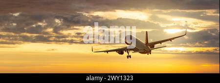 Aereo. Paesaggio con grande aereo passeggeri bianco sta volando nel cielo giallo al tramonto colorato. Viaggio. Gli aerei passeggeri atterrano al tramonto Foto Stock