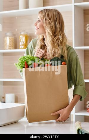 Una donna che tiene una borsa della spesa piena di verdure fresche in cucina. Foto Stock