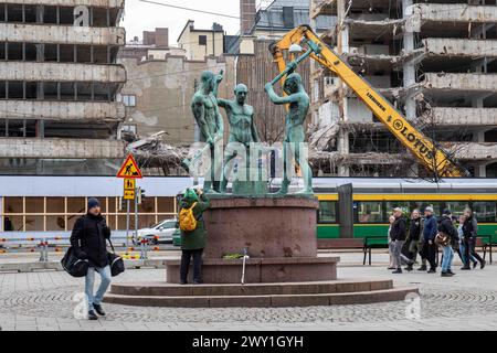 Scultura dei tre fabbri con edificio per uffici Aktian talo in fase di demolizione sullo sfondo nel quartiere Kluuvi di Helsinki, Finlandia Foto Stock