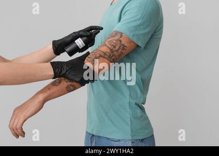 Maestro del tatuaggio che spruzza il braccio dell'uomo su sfondo chiaro, primo piano Foto Stock