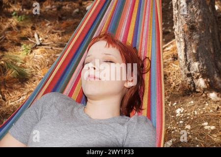 ritratto di un'adolescente addormentata con i capelli rossi su un'amaca nella foresta. Foto Stock