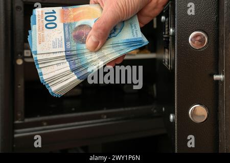 Mettere un pacchetto di denaro in una cassaforte aperta o estrarlo. Le barre di bloccaggio della porta di sicurezza aperta sono visibili in primo piano. Foto Stock
