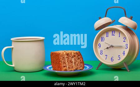 Concetto di tempo del caffè con tazza di caffè, sveglia e un pezzo di torta con sfondo colorato. Foto Stock