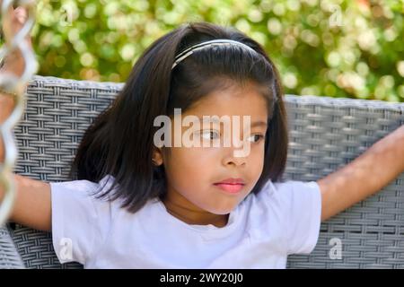 Un ritratto ravvicinato di una giovane ragazza asiatica con un'espressione gioiosa sul viso, perduta nella meraviglia nel verde vibrante di un bellissimo giardino Foto Stock