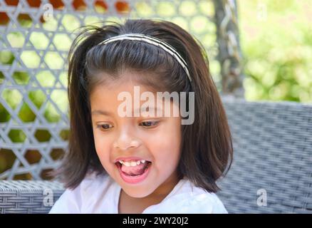 Un ritratto ravvicinato di una giovane ragazza asiatica con un'espressione gioiosa, che esplora giocosamente un vivace giardino verde. Foto Stock