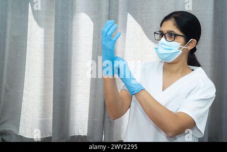 Una donna che indossa un camice da laboratorio bianco e guanti blu indossa una maschera. Concetto di cautela e responsabilità, in quanto la donna sta prendendo la necessaria precauzione Foto Stock