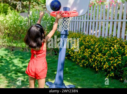 Una bambina con un'espressione decisa bagna una pallacanestro in una giornata di sole nel suo cortile Foto Stock