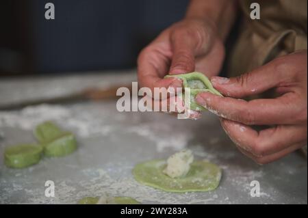 Le mani da vicino di una donna nella cucina rurale, scolpiscono gnocchi di impasto con ripieno di purè di patate. Cucinare deliziosi gnocchi vegetariani fatti in casa Foto Stock