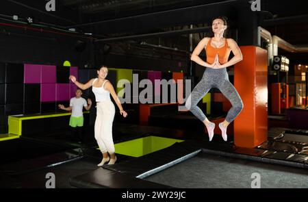 Donna di mezza età felice che pratica e salta sui trampolini in un centro sportivo al coperto, allenamento e moderno concetto di intrattenimento Foto Stock