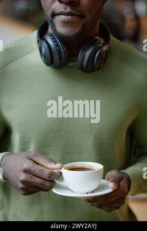 Primo piano verticale di un giovane afroamericano che regge una semplice tazza di caffè contro una camicia girocollo verde Foto Stock