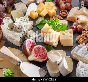 Varietà di formaggi a fette con frutta, menta, noci e taglierini. Un meraviglioso sfondo di formaggi per i vostri progetti. Foto Stock